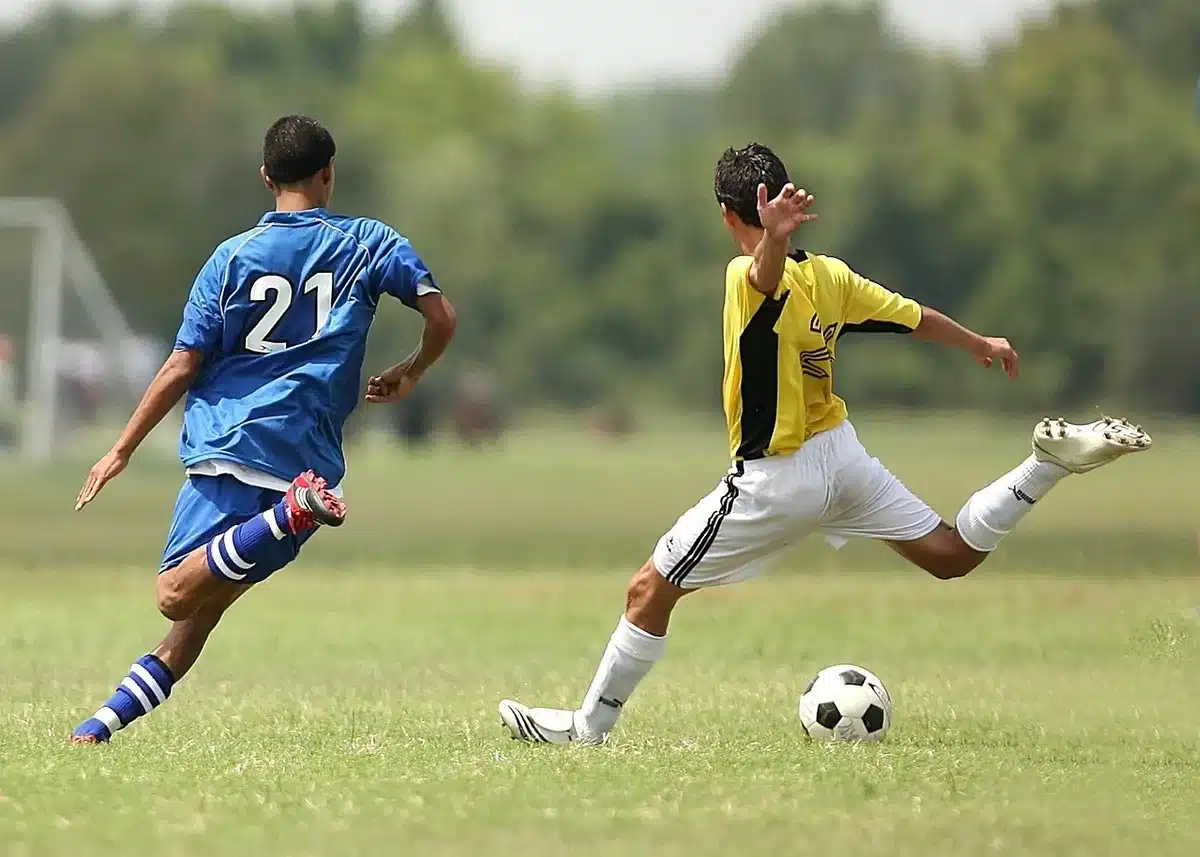 Giocatore di calcio in azione durante una partita, con sullo sfondo bandiere di squadre diverse