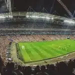 Silhouette di scarpe da calcio e pallone sul prato illuminato dallo stadio