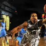 Due giocatori di basket in azione in campo durante una partita, uno in difesa e uno in attacco.