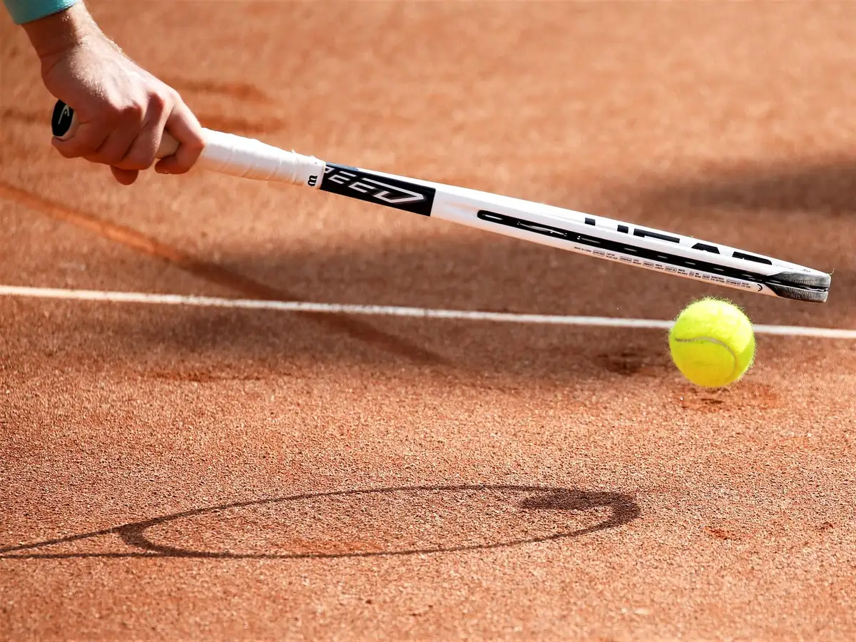 Silhouette di un giocatore che serve su un campo da tennis, vista dalla linea di fondo