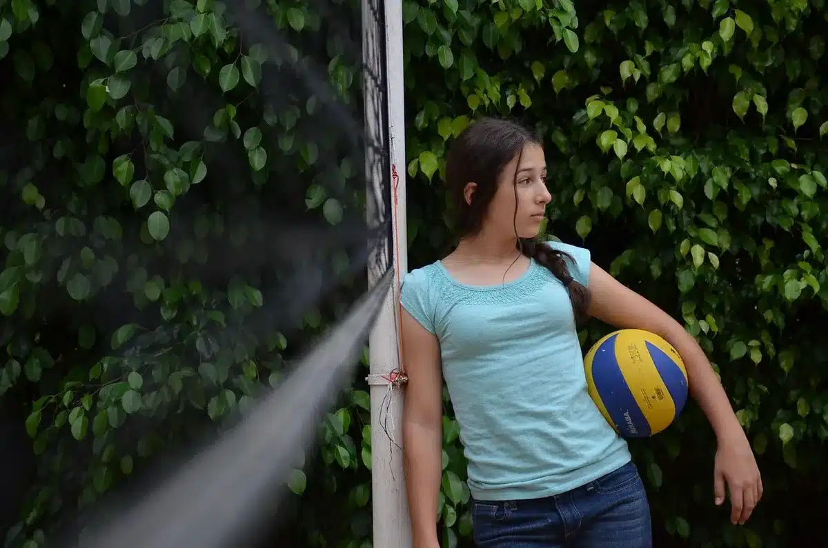 Interno di palazzetto con rete da pallavolo, mani in aria e pubblico sfocato sugli spalti