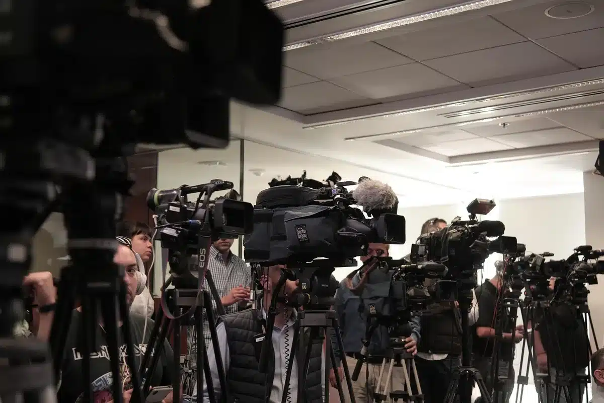 Conferenza stampa con pilota al microfono e giornalisti sullo sfondo